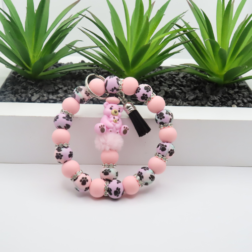 Pink beaded bracelet with a heart charm on a white surface with green plants in the background
