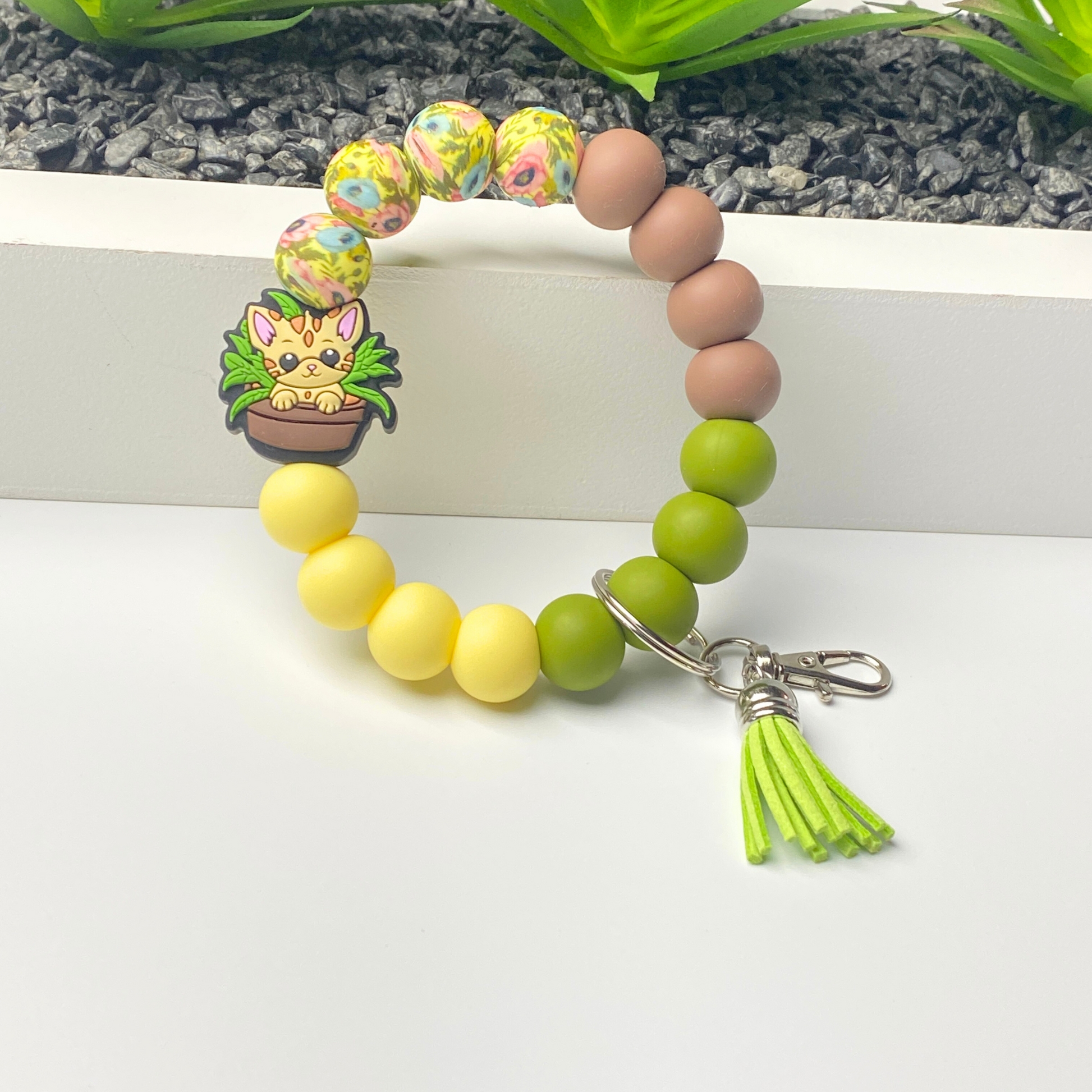 Beaded bracelet with yellow, green, and brown beads, a keychain charm, and a tassel on a white background.
