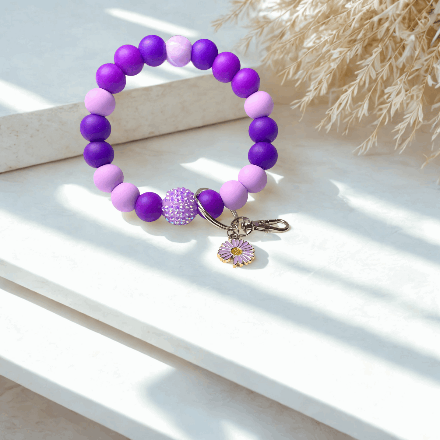 Purple and pink beaded bracelet with a floral charm on a white surface