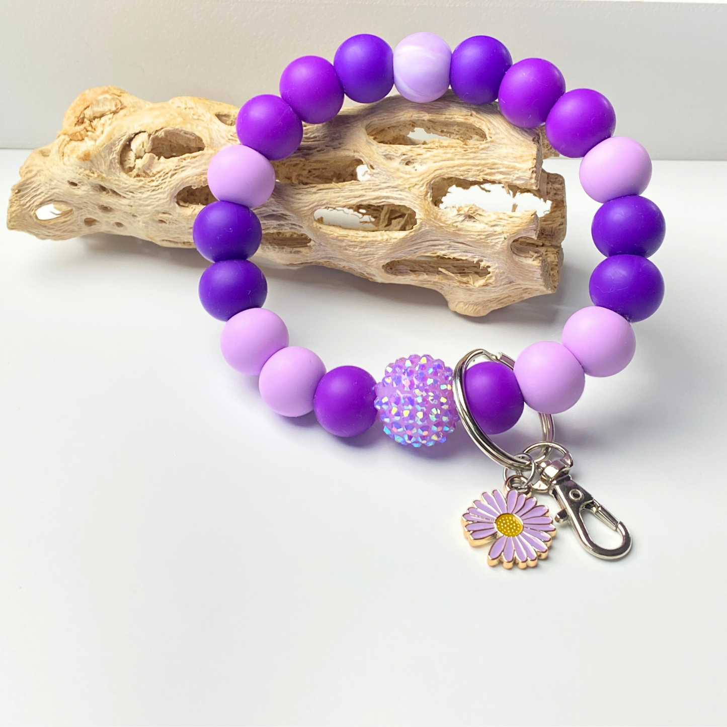 Purple and pink beaded bracelet with a keychain charm on a light background