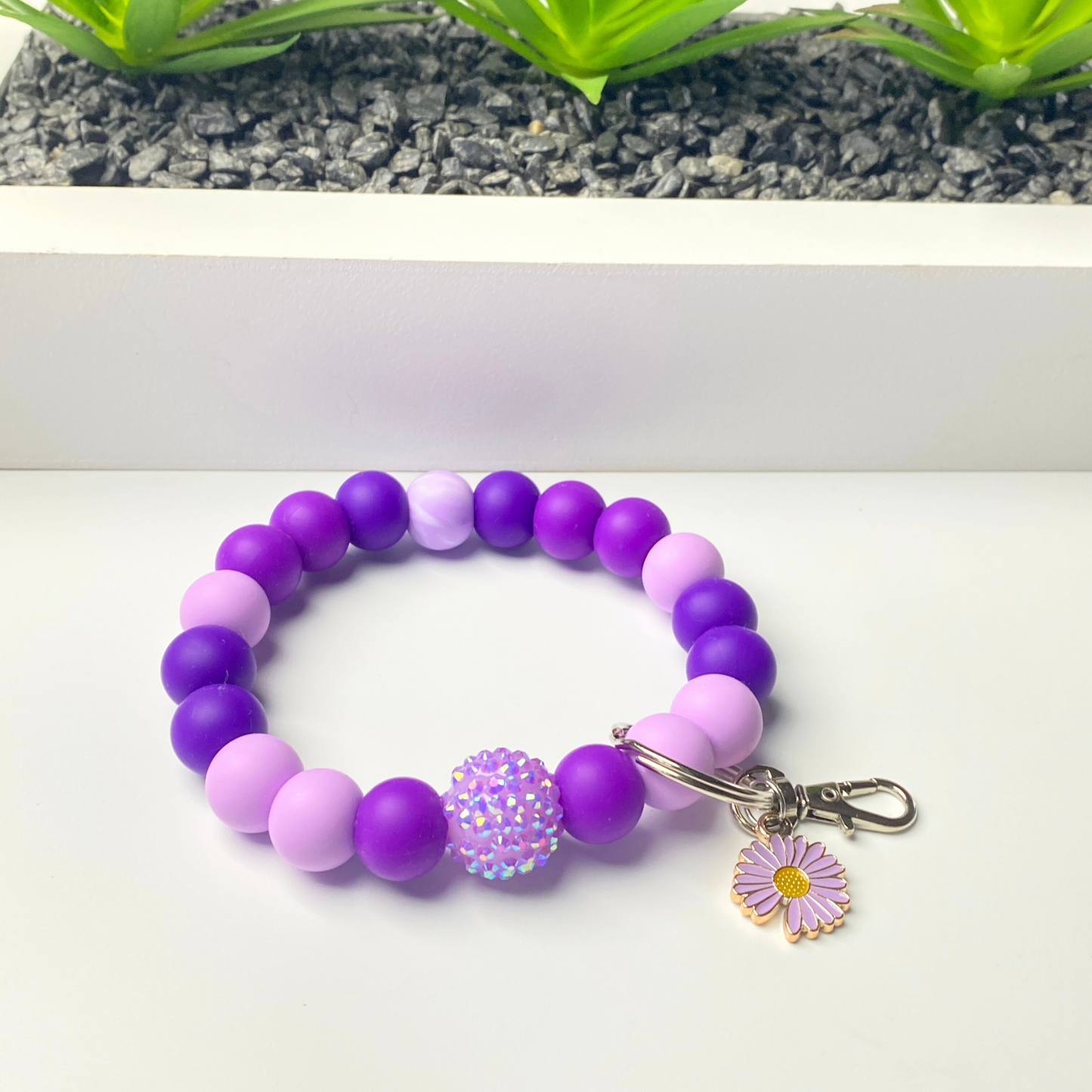 Purple beaded bracelet with a floral charm on a white background