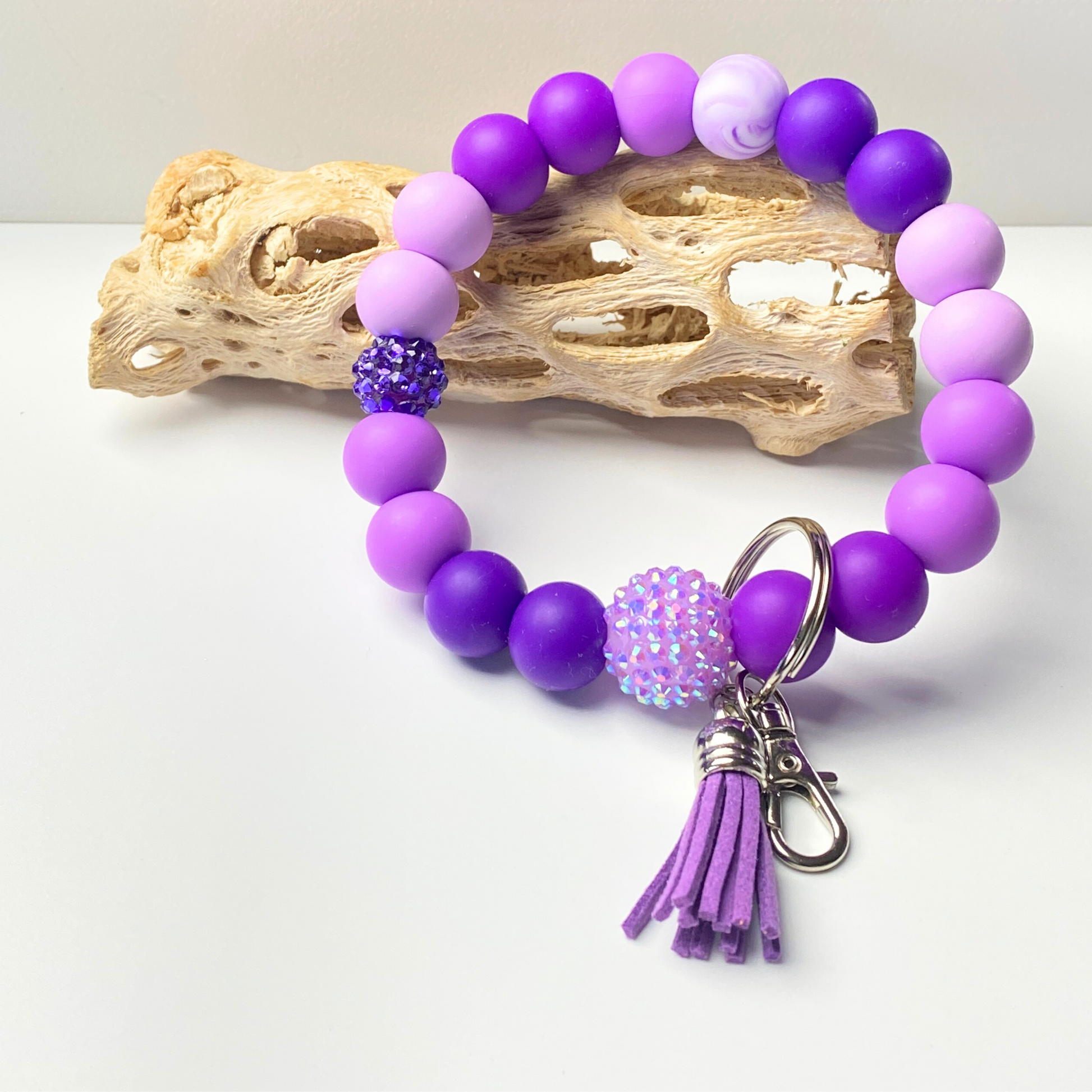 Purple beaded bracelet with a tassel charm on a white background