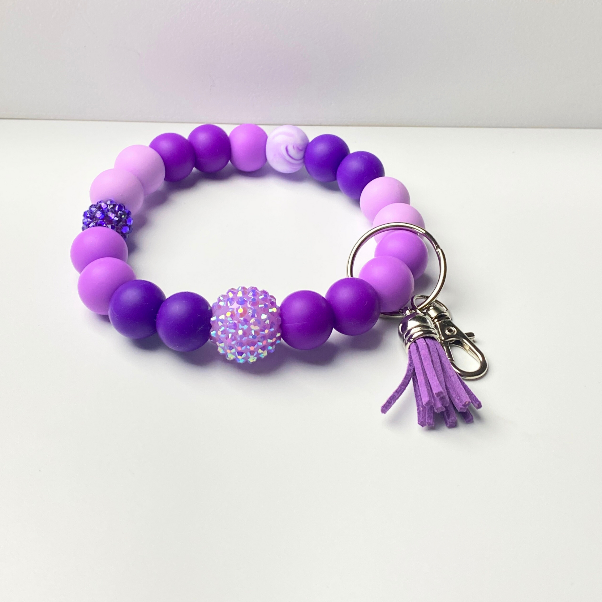 Purple beaded bracelet with a keychain and tassel on a white background