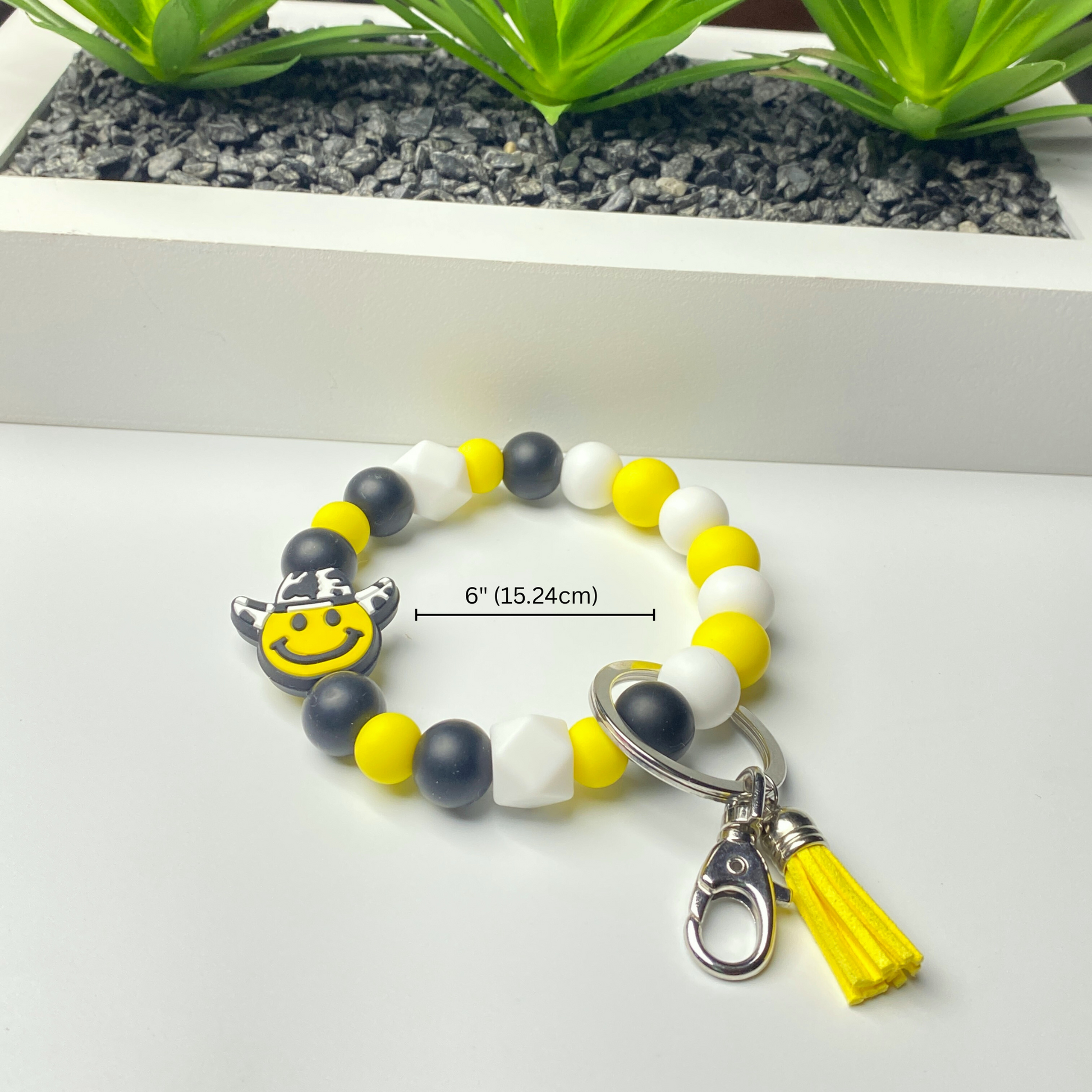 Bracelet with smiley face charm and tassel on a white surface with plants in the background
