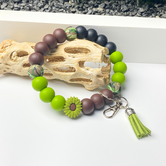 Beaded bracelet with green and brown beads and a tassel charm on a white surface.