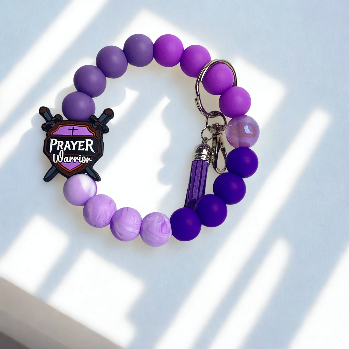 Purple beaded bracelet with a 'Prayer Warrior' charm on a light background