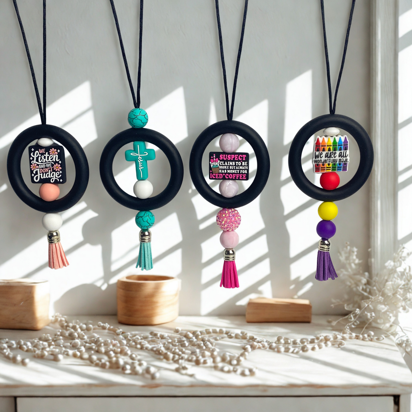 Four necklaces with round black beads and colorful tassels on a white surface with sunlight filtering through.