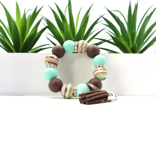 Beaded bracelet with turquoise and brown beads on a white surface with green plants in the background