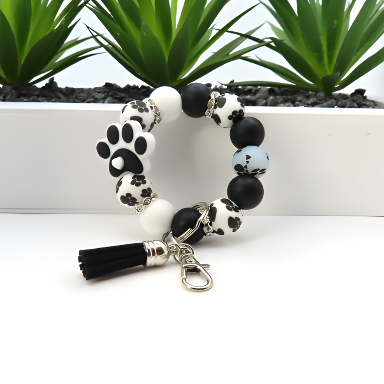 Bracelet with paw print design and tassel on a white surface with plants in the background