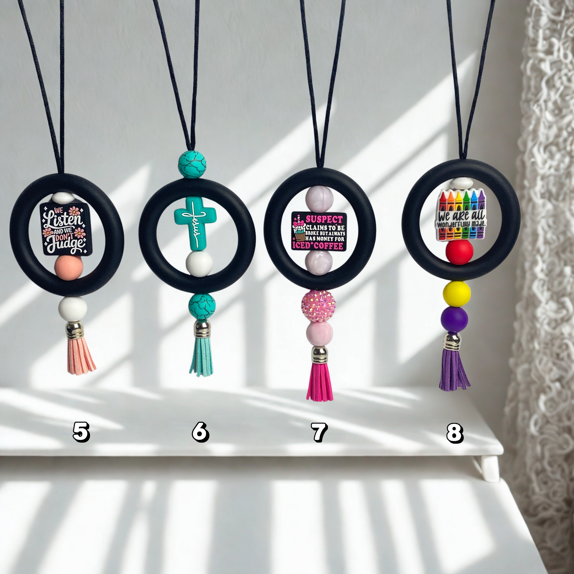 Four necklaces with circular pendants and colorful tassels on a white surface.