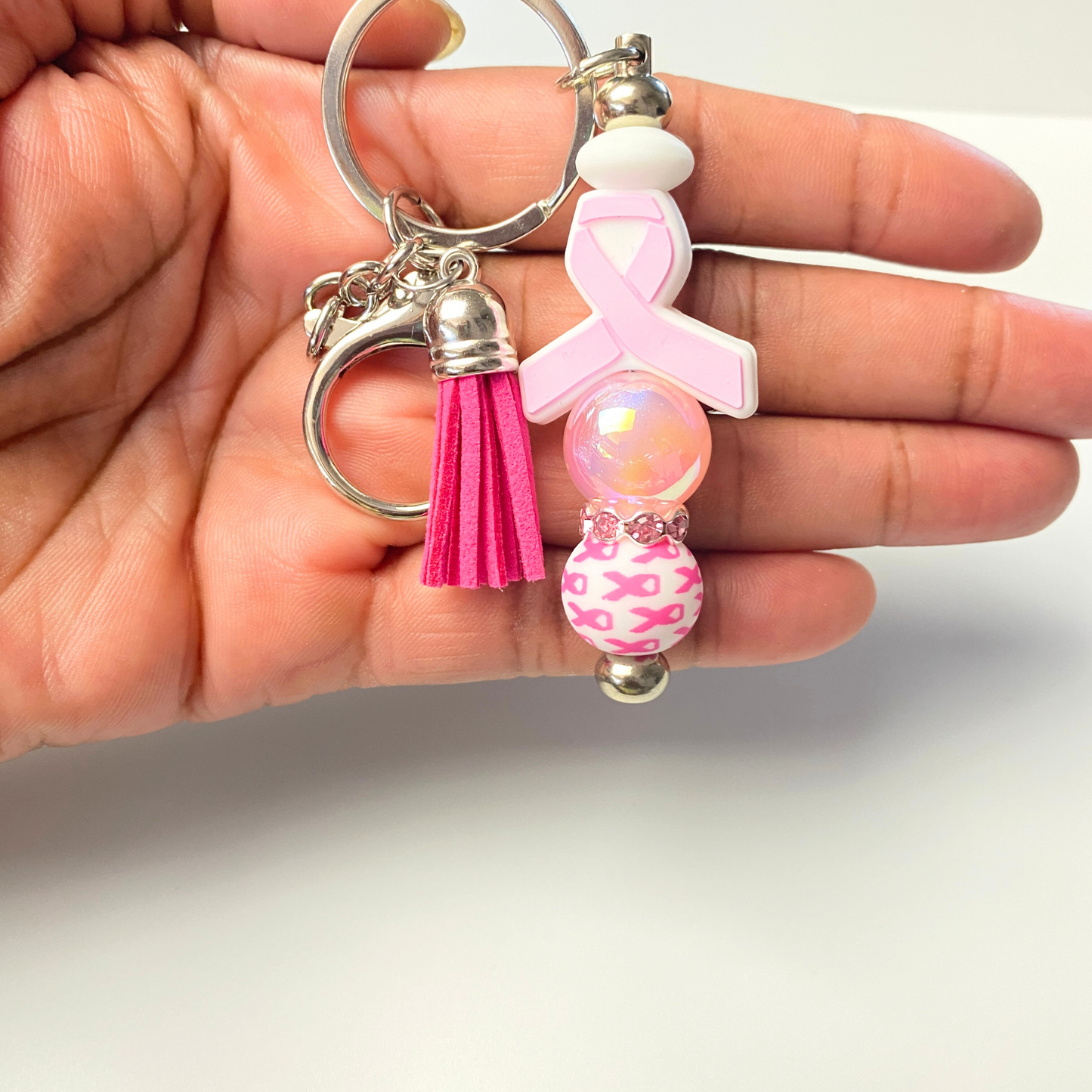 Pink keychain with breast cancer awareness ribbon held in a hand against a white background