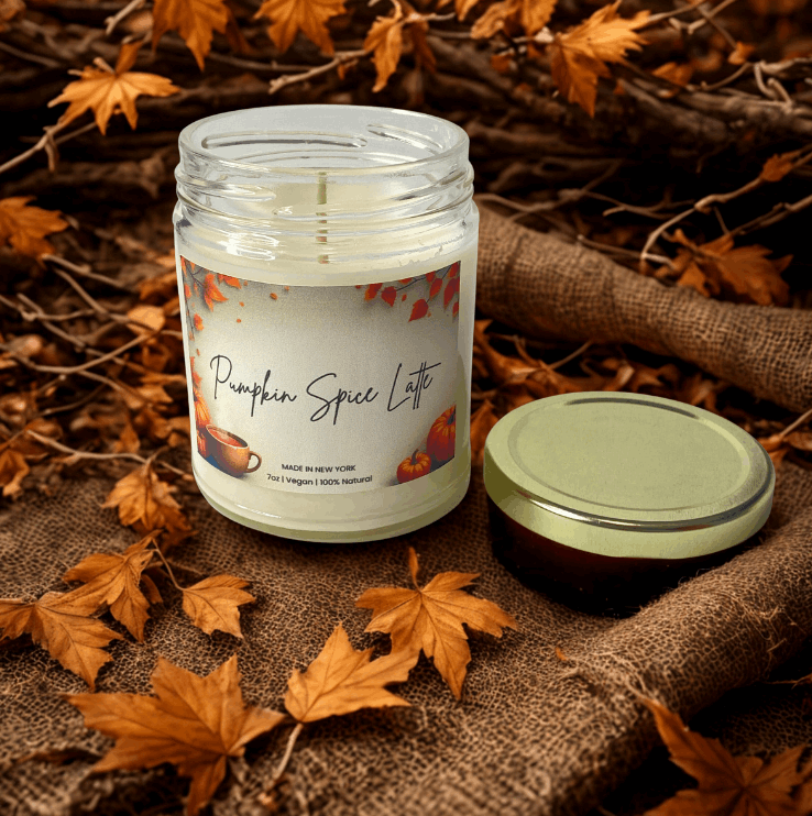 Pumpkin spice latte candle in a jar with a label on a burlap surface with autumn leaves.