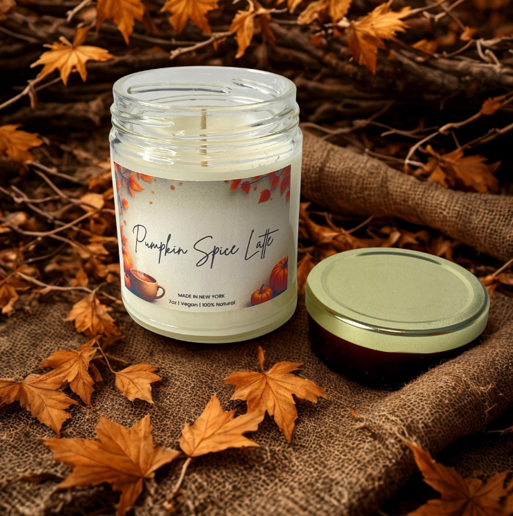 Pumpkin spice latte candle in a jar with a label on a burlap surface with autumn leaves.