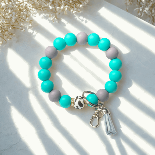 Beaded bracelet with teal and gray beads and a keychain on a light background