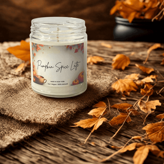 Candle labeled 'Pumpkin Spice Latte' on a wooden surface with autumn leaves.