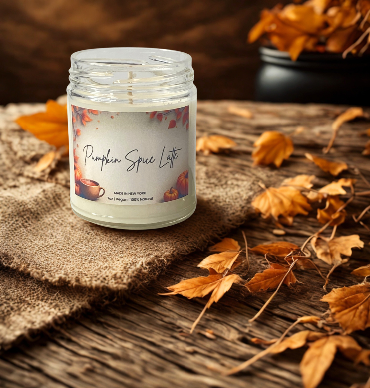 Candle labeled 'Pumpkin Spice Latte' on a wooden surface with autumn leaves.