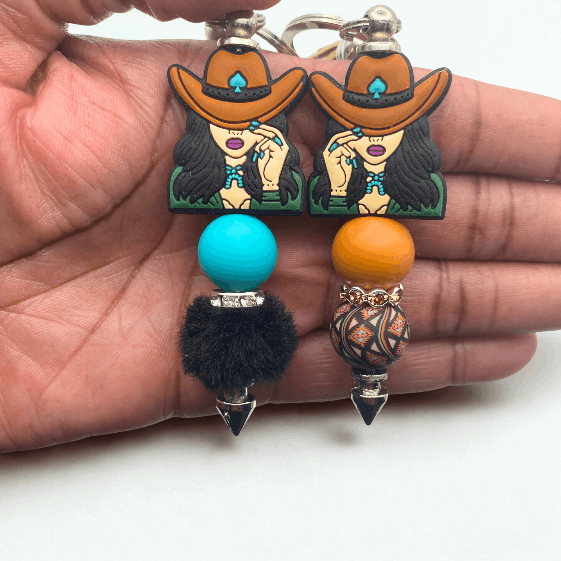 Pair of earrings with cowboy hats and colorful beads held in a hand.