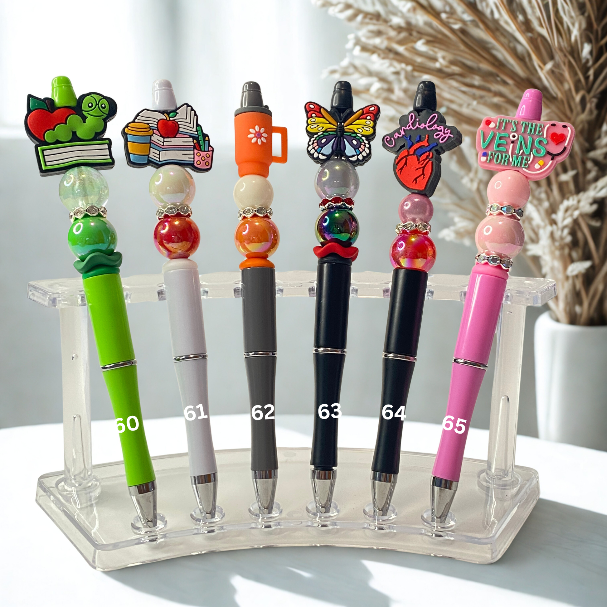 Set of colorful pens with decorative tops on a clear stand.