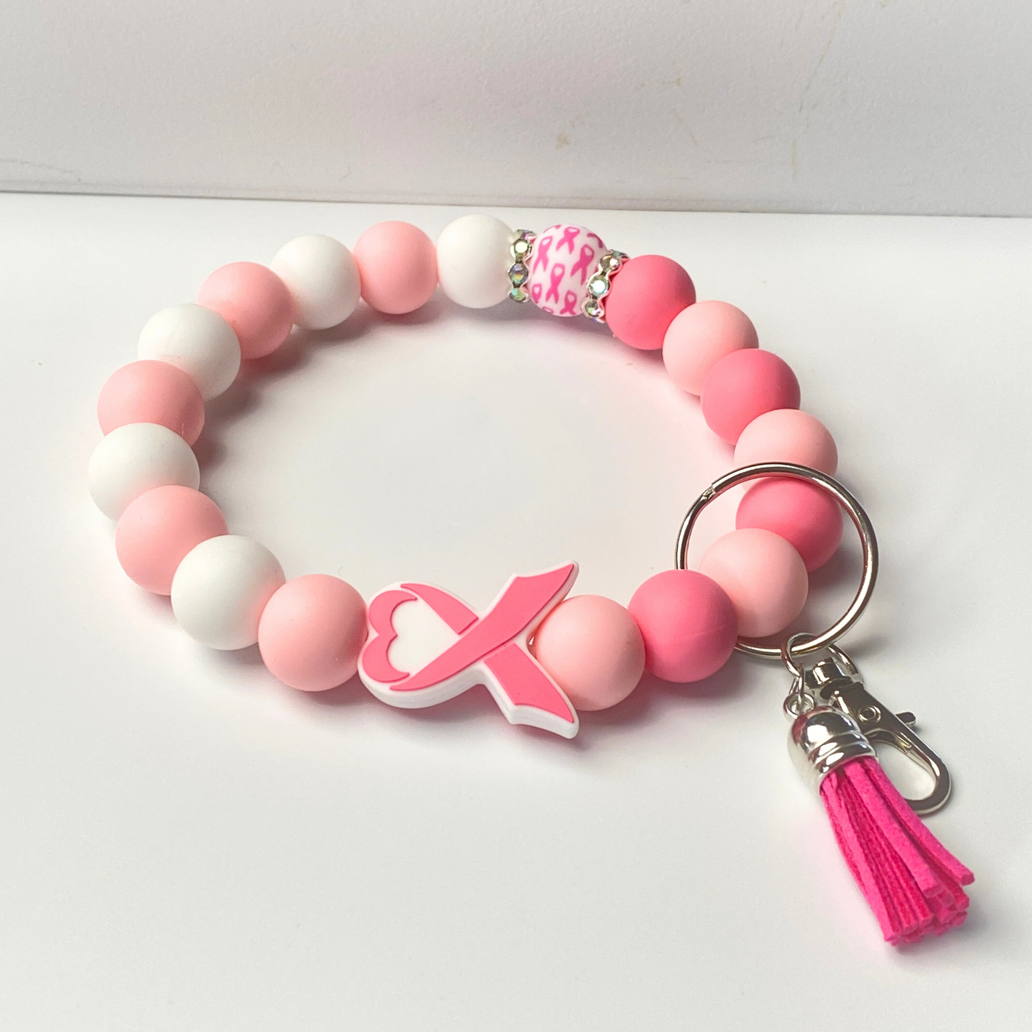 Pink and white beaded bracelet with a pink heart charm and tassel on a white background