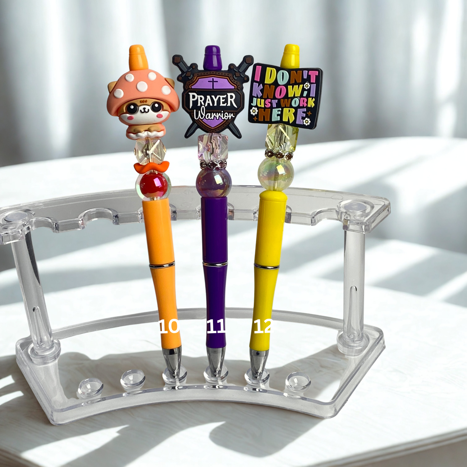 Three colorful pens with decorative tops on a clear stand against a white background