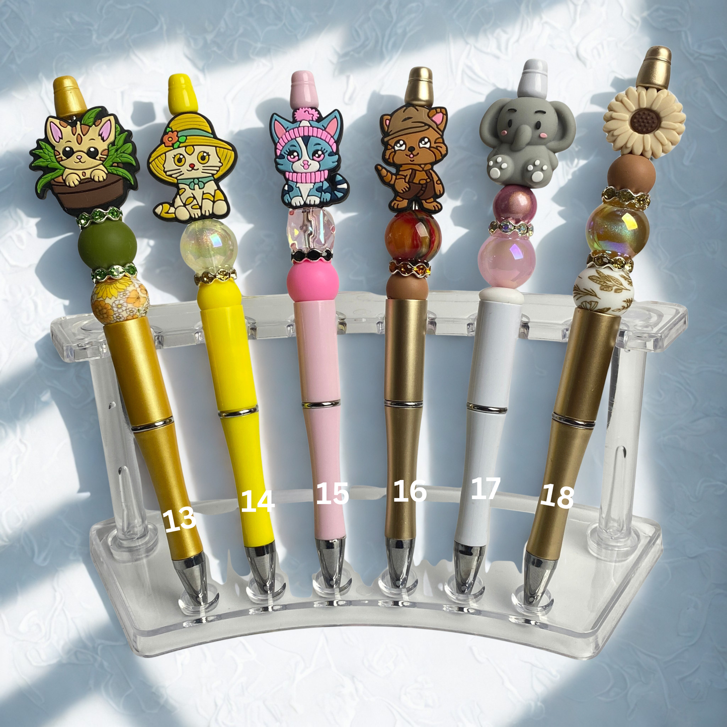 Set of colorful pens with cartoon character tops on a clear stand against a light blue background.