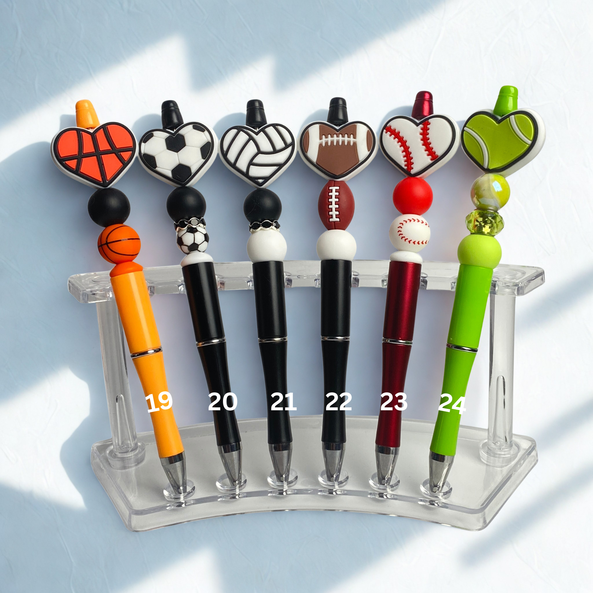 Set of sports-themed pens on a clear stand against a light blue background