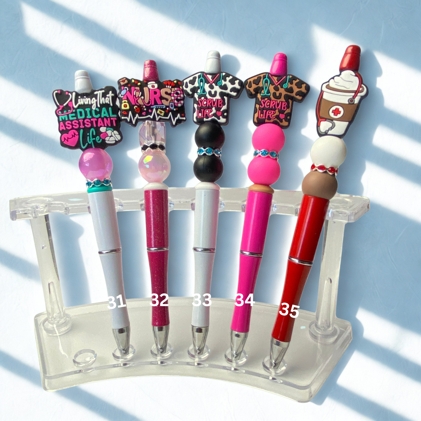 Set of pens with decorative tops on a clear stand against a light blue background