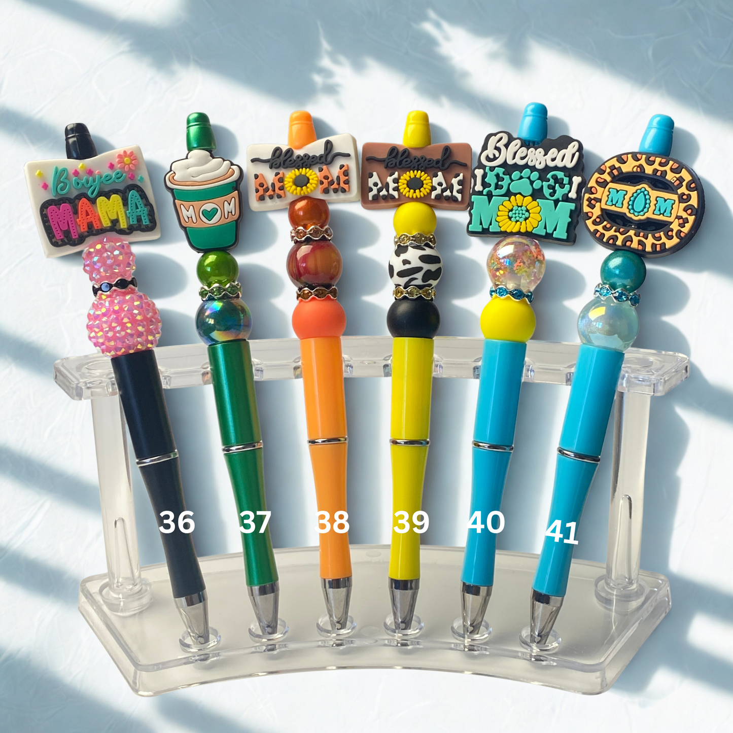 Colorful pens with decorative tops on a clear stand against a white background
