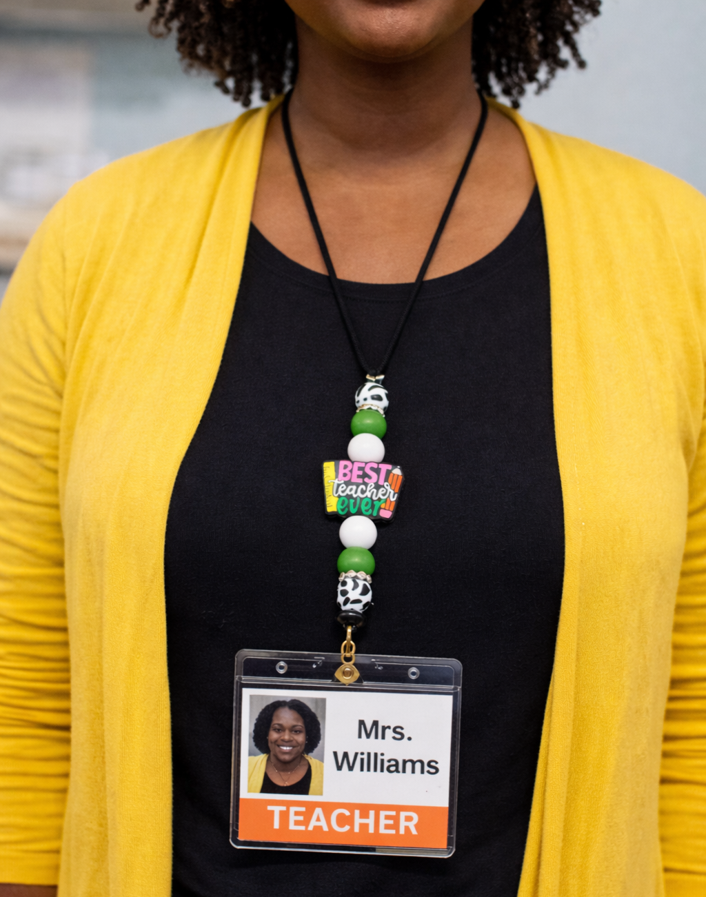Person wearing a black shirt with a teacher name tag and yellow cardigan.