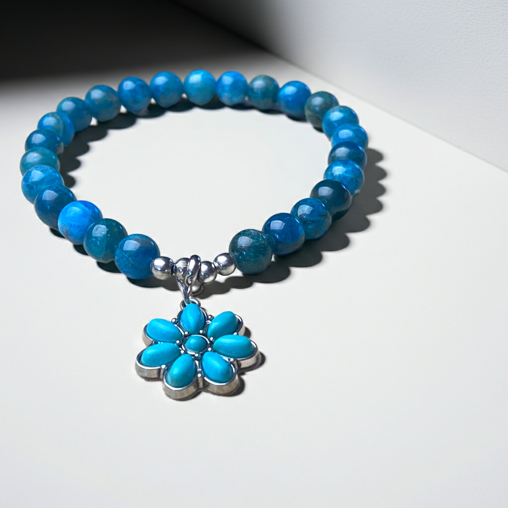 Blue beaded bracelet with a silver and turquoise flower charm on a white surface.