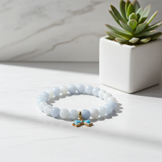Beaded bracelet with a gold and blue charm on a marble surface with a succulent plant in the background.