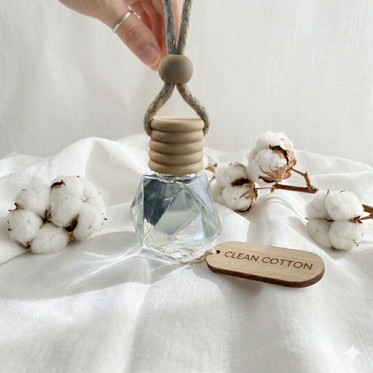 Perfume bottle with wooden cap and 'Clean Cotton' tag on a white fabric background with cotton flowers.