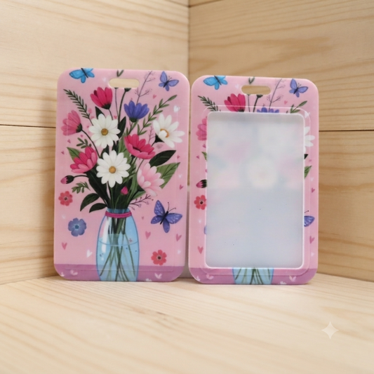 Two pink phone cases with a floral and butterfly print, displayed on a light wood surface against a wood-paneled background.