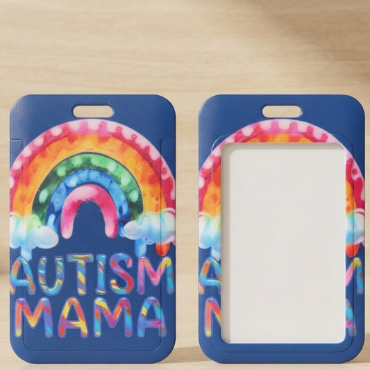 Two blue ID badge holders with a colorful rainbow and the words 'AUTISM MAMA' are shown on a light wood surface. One holder is front-facing, showing the printed design, and the other is back-facing with a blank white insert area.