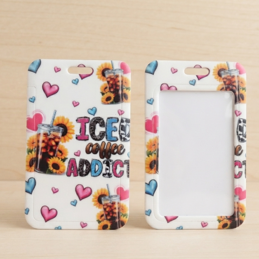 Two white phone cases with a colorful 'ICE coffee ADDICT!' graphic and sunflower/heart pattern, displayed side-by-side on a light wood background.