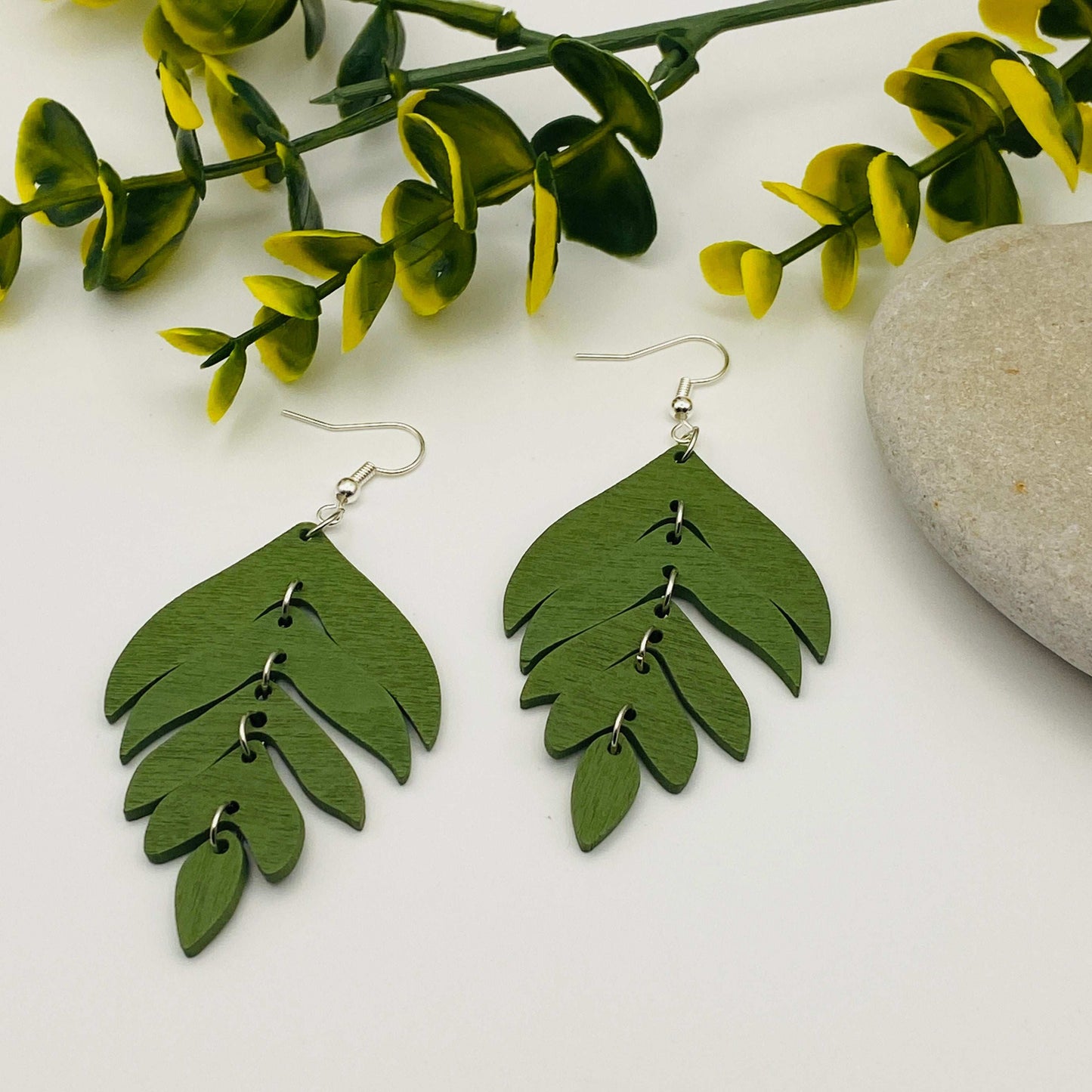Green leaf-shaped earrings on a white background with green leaves and a stone.