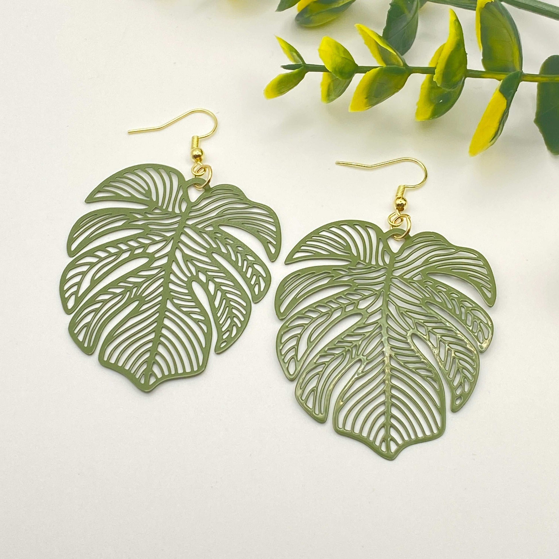 Green leaf-shaped earrings on a white background with green leaves.