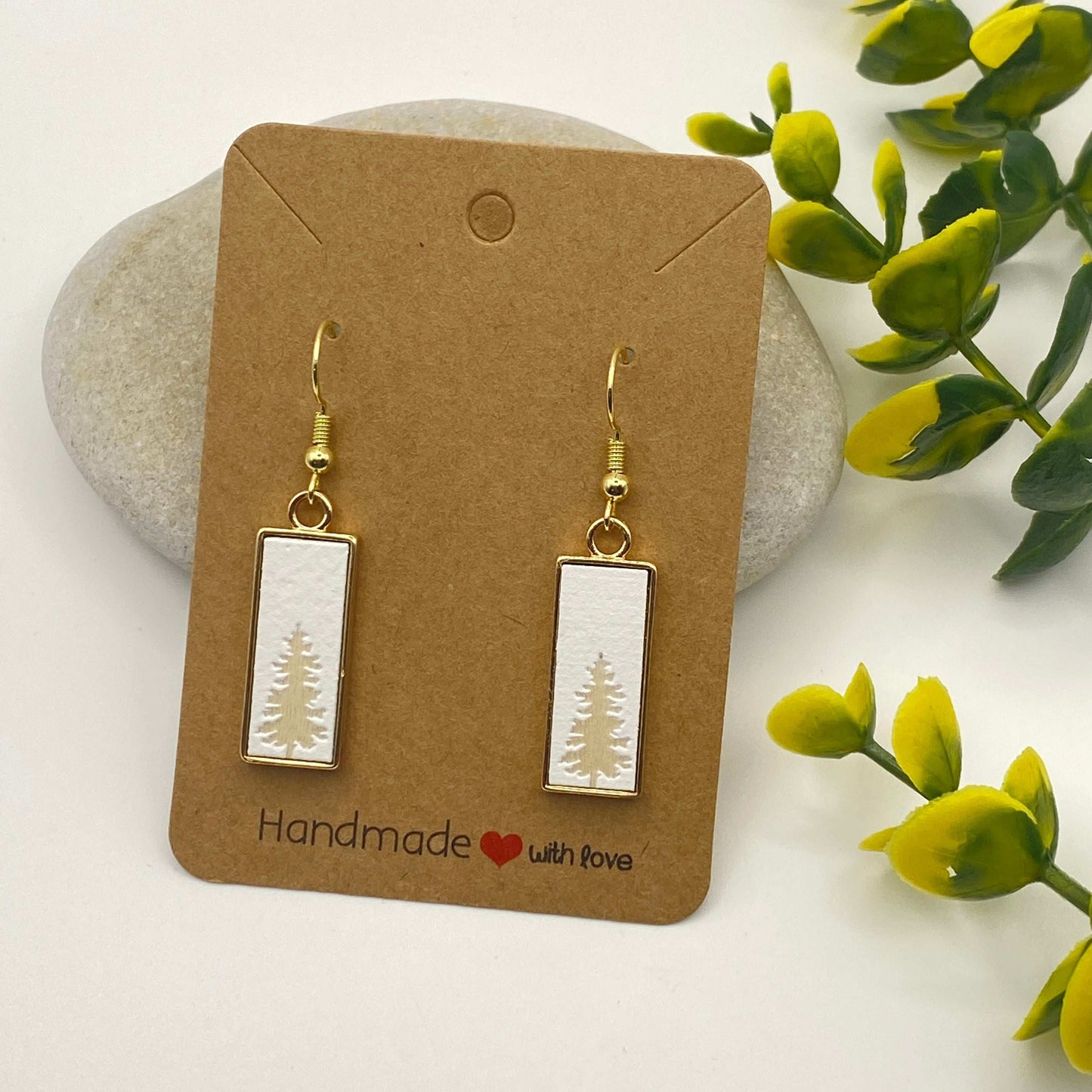Rectangular earrings with tree design on a 'Handmade with Love' card, surrounded by stones and greenery.