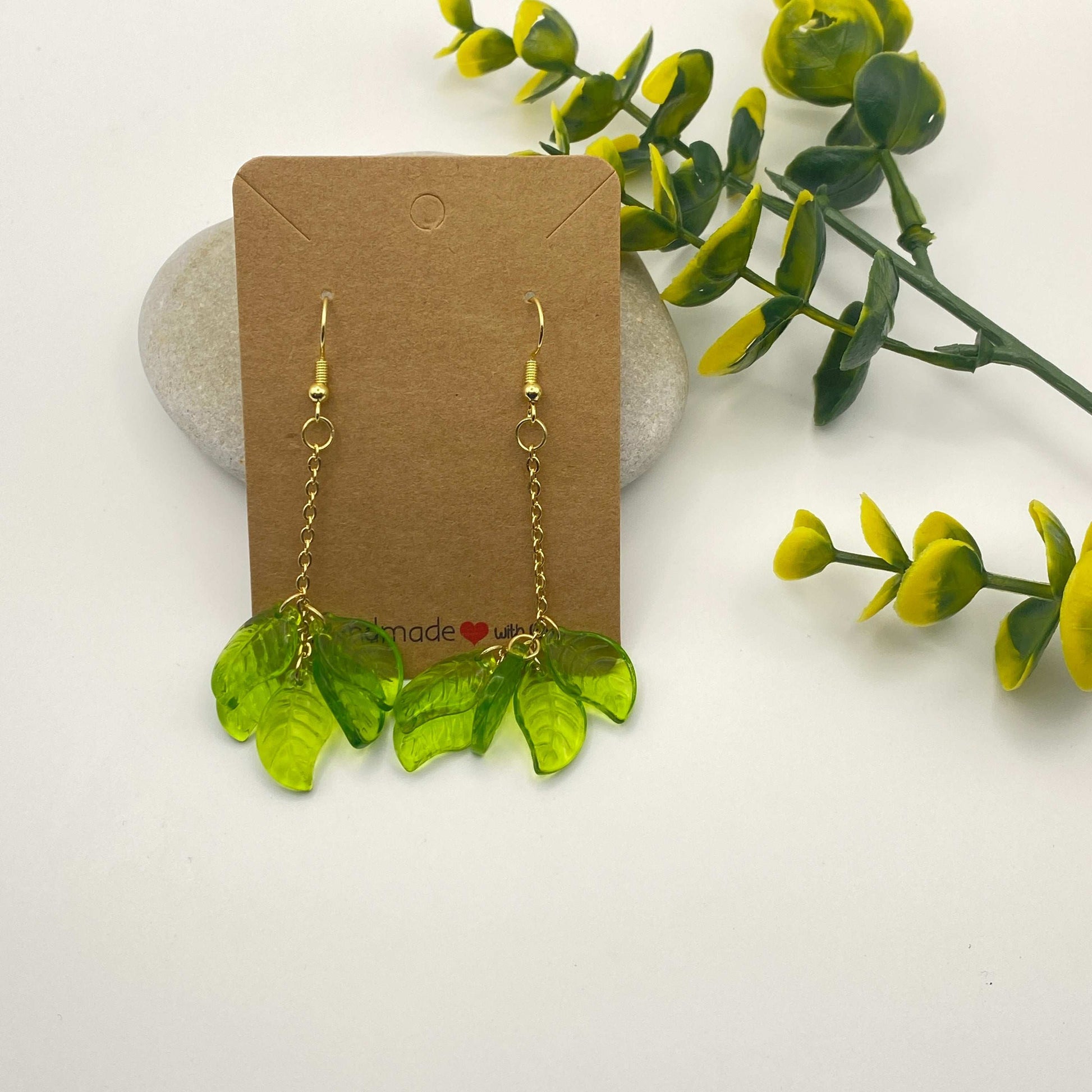 Green leaf-shaped earrings on a brown card with a white background and green leaves.