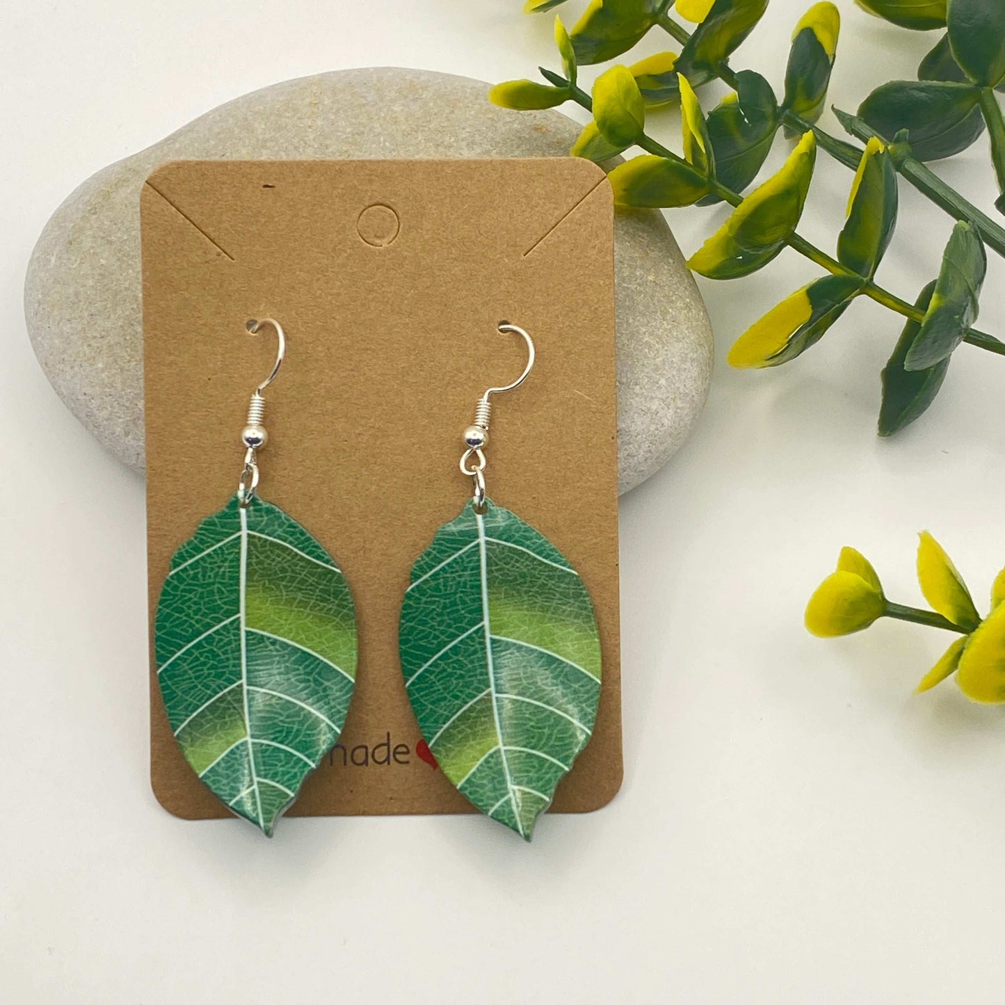 Green leaf-shaped earrings on a brown card with a natural background