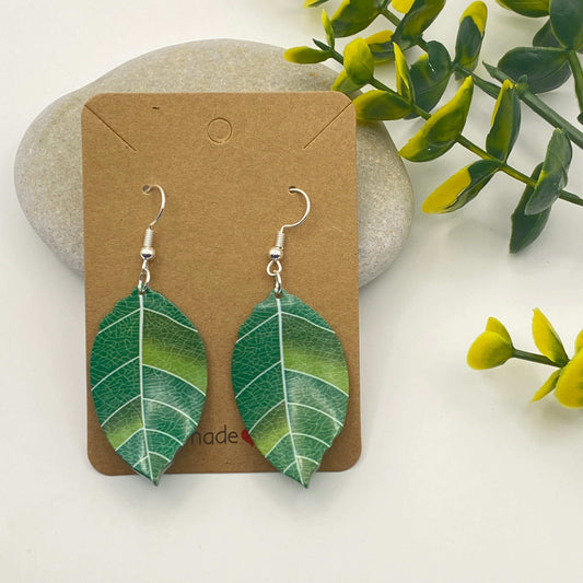 Green leaf-shaped earrings on a brown card with a natural background