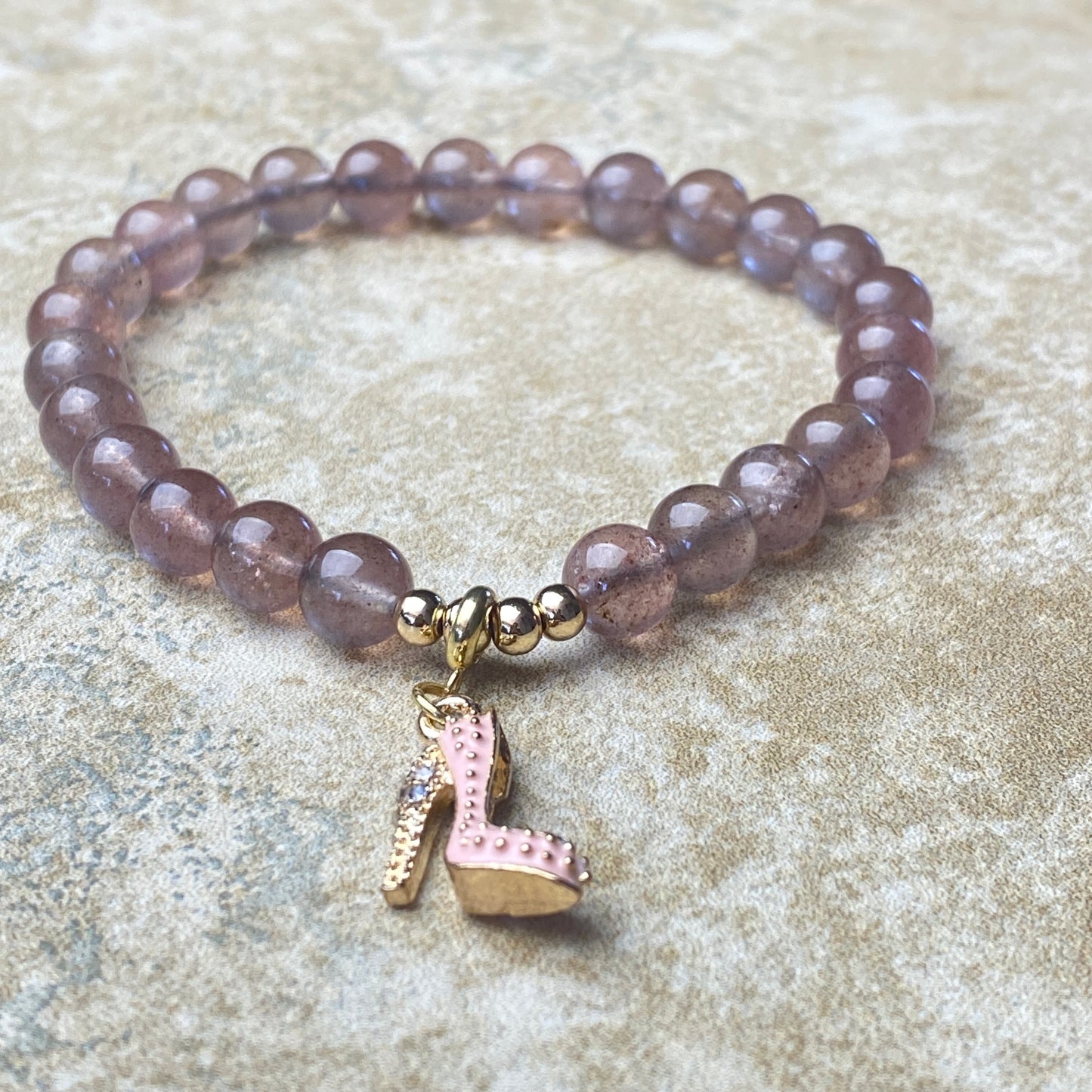 Beaded bracelet with a pink shoe charm on a textured surface