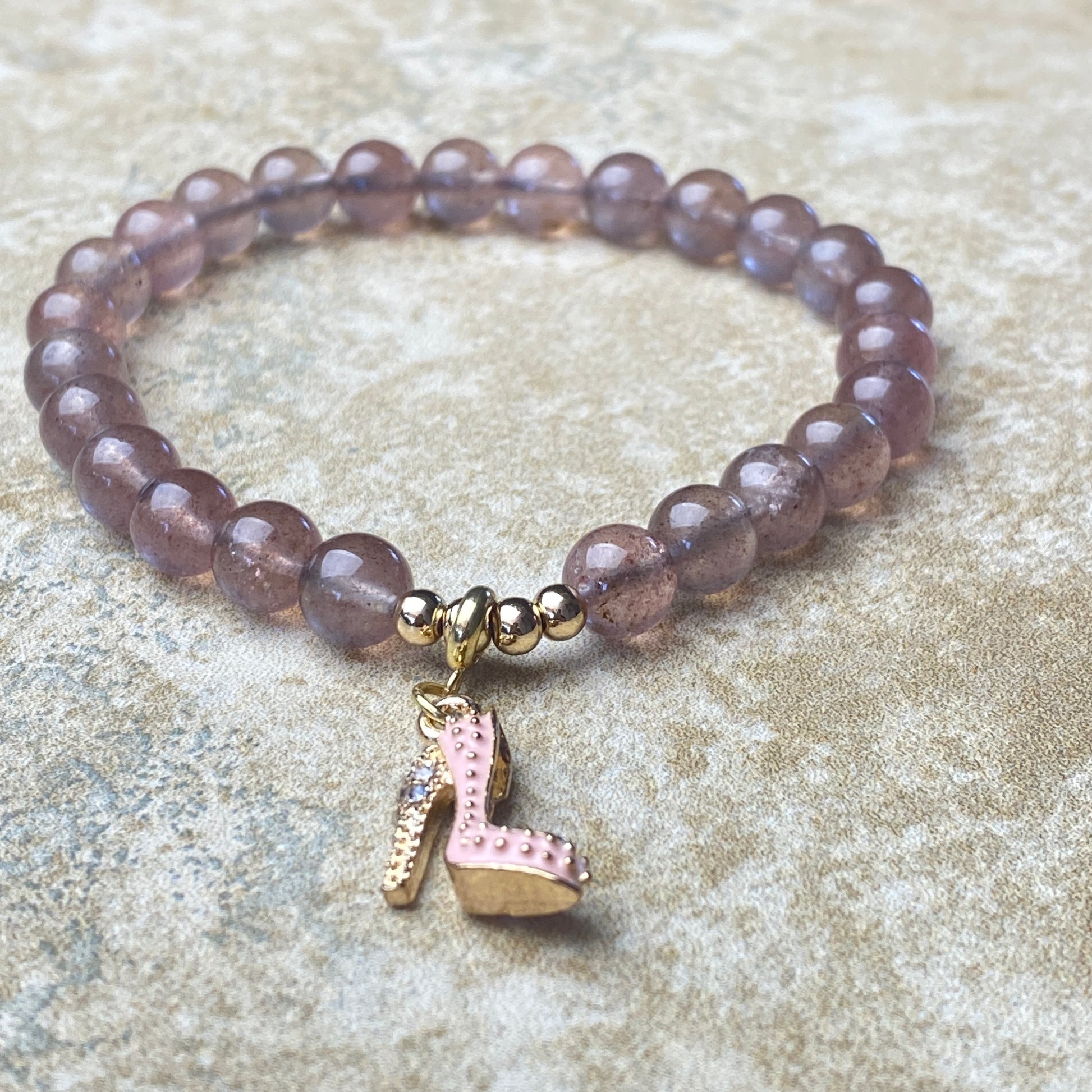Beaded bracelet with a pink shoe charm on a textured surface