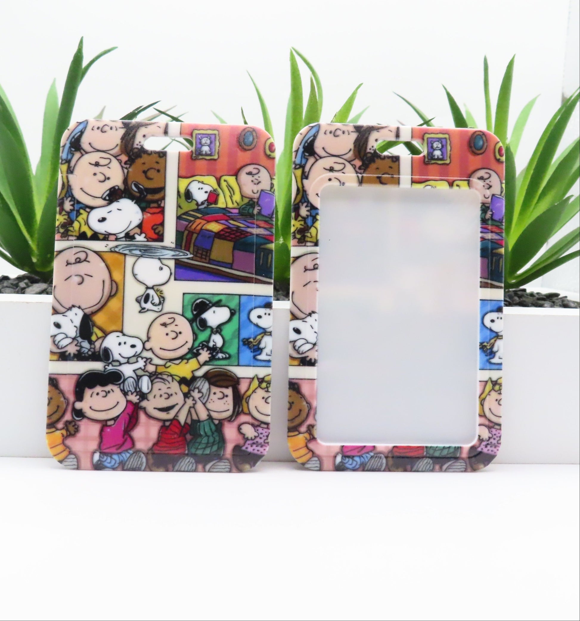 Phone case with cartoon design featuring characters and a colorful background, placed on a white surface with green plants.