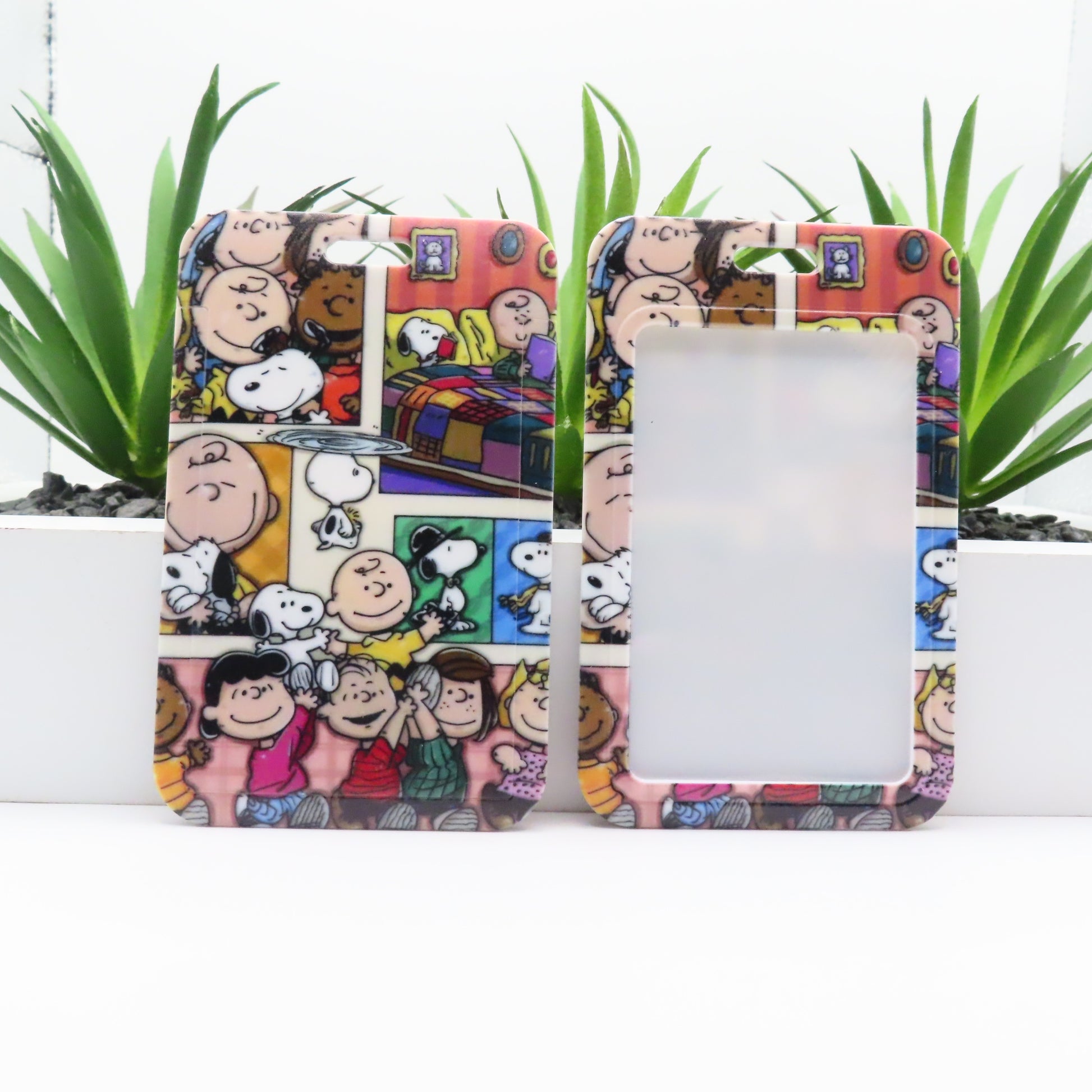 Phone case with cartoon design featuring characters and a colorful background, placed on a white surface with green plants.