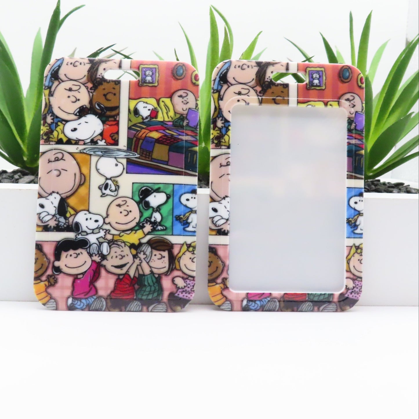 Phone case with cartoon design featuring characters and a colorful background, placed on a white surface with green plants.
