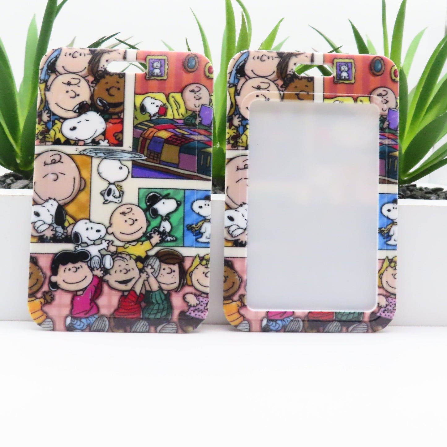 Phone case with cartoon design featuring characters and a colorful background, placed on a white surface with green plants.