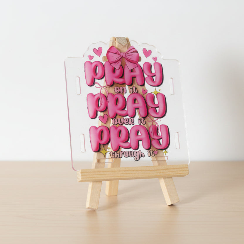 Decorative sign with pink text 'PRAY ON IT PRAY OVER IT PRAY THROUGH IT' on a white background