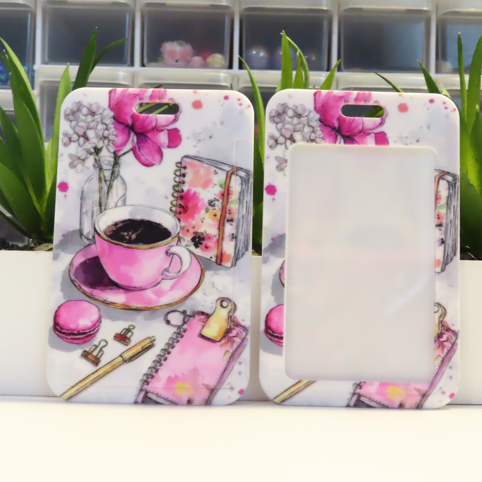 Two phone cases with floral and tea design on a white surface with plants in the background.