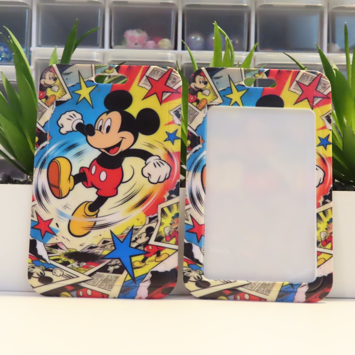 Colorful phone case with Mickey Mouse design on a white surface with green plants in the background.